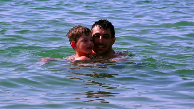 Joven-padre-con-un-hijo-pequeño-en-la-playa-de-la-mar,-Grecia