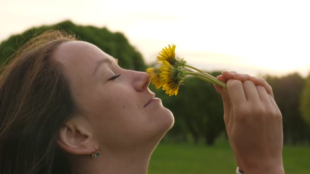 Woman-smells-dandelions-at-sunset,-face-close-up