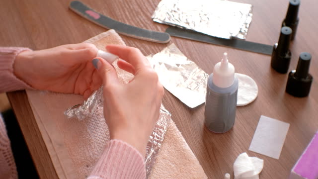 Removing-gel-Polish-from-nails.-Woman-pours-remove-liquid-on-a-cotton-pad,-puts-it-on-a-nail-and-wraps-the-foil.-Close-up-hands.-All-fingers-with-foil.