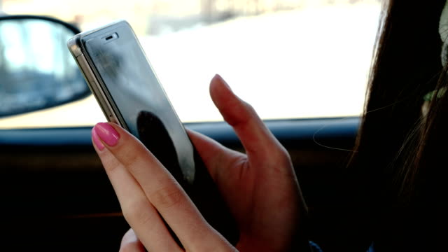 Close-up-Frauenhand-messaging-ihr-Handy-im-Auto-zu-sitzen.-Seitenansicht.