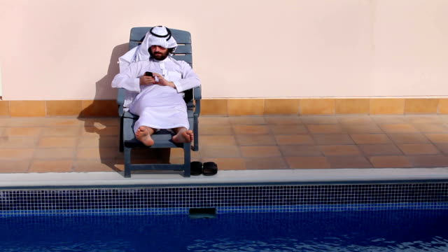 saudi-arabischer-Mann-mit-seinem-Handy-am-Swimmingpool