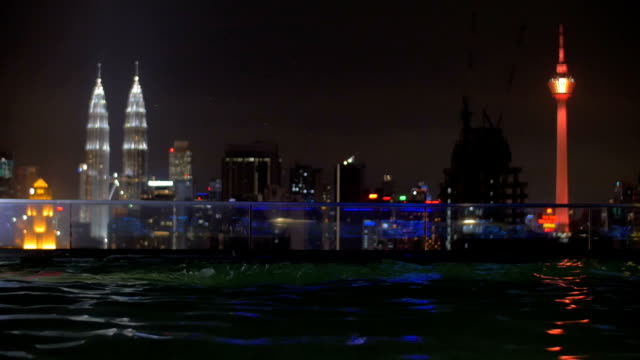 Mujer-relajante-en-la-piscina-en-la-azotea-por-la-noche,-Kuala-Lumpur