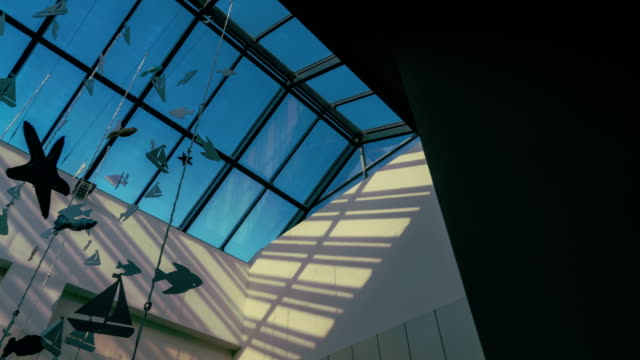 Schwenk-in-der-Glasdecke-des-Shopping-Centers-mit-Papier-Girlanden-auf-einem-Hintergrund-von-Time-Lapse-Licht-der-Sonnenstrahlen-auf-einen-blauen-Himmel