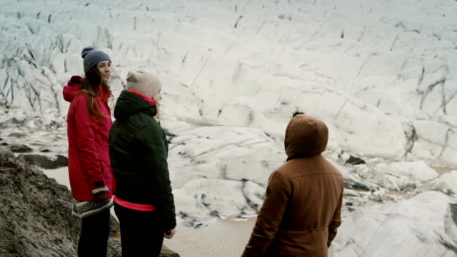 Group-of-young-people-standing-on-the-mountain-and-showing-to-something,-walking-in-Vatnajokull-ice-lagoon-in-Iceland