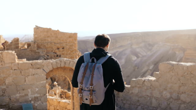 Hombre-europeo-explora-paisajes-montañosos-antiguos.-Joven-turista-masculino-con-cámara-y-mochila-toma-fotos.-Israel-4K