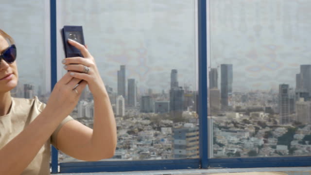 Mujer-sonriente-haciendo-foto-de-celular-contra-Tel-Aviv-vista-desde-la-altura