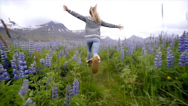Young-woman-running-in-flower-lupine-field-in-Iceland-living-a-happy-life-and-enjoying-vacations-in-northern-country--Slow-motion-video-people-travel-fun-concept