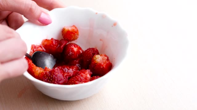 Woman-kneads-strawberries-with-a-spoon-and-mixes-it-with-sugar,-making-jam.-Close-up-hand.
