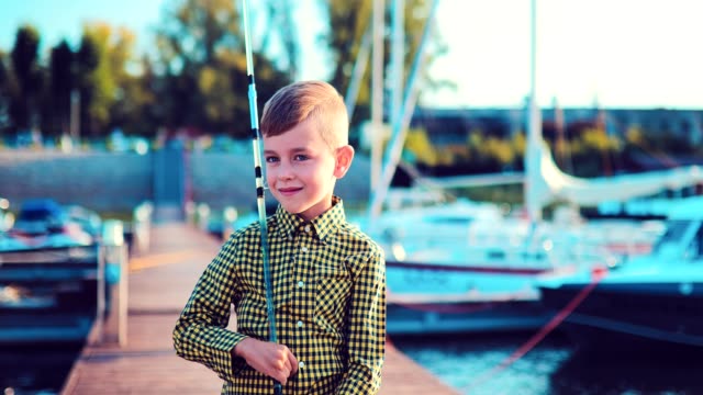 Kleiner-Junge-mit-einer-Angelrute-steht-auf-einem-Dock-in-der-Nähe-von-Booten-und-Yachten