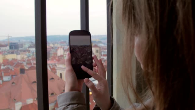 young-woman-is-enjoying-Prague-view-from-Old-Town-Hall-and-taking-photos-by-smartphone