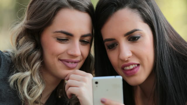 Echte-Freunde-zusammen-im-freien-Handy-überprüfen.-Mädchen-auf-der-Suche-und-halten-Smartphone-chatten-Klatsch-austauschen