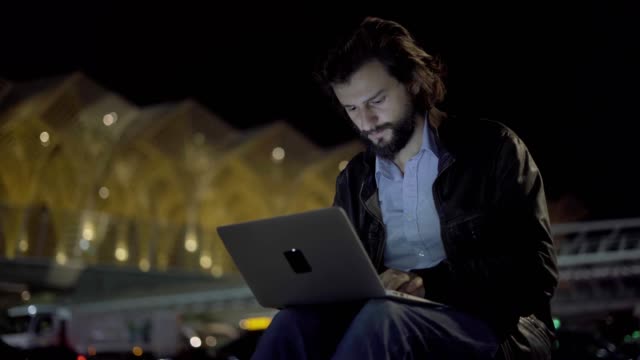 Young-confident-man-typing-on-laptop-in-night-city