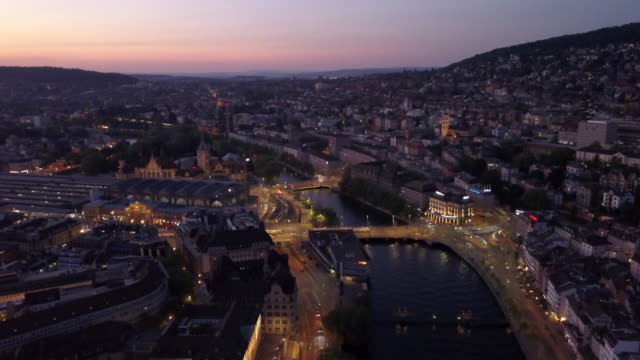 puesta-de-sol-iluminada-Zurich-centro-ciudad-orilla-aérea-panorama-4k-Suiza