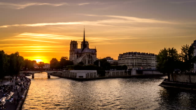 Timelapse-of-boats-in-Paris-at-sunset,-with-Notre-Dame-De-Paris-church-in-the-background-and-people-resting-on-the-docks,-view-from-Tournelle-bridge