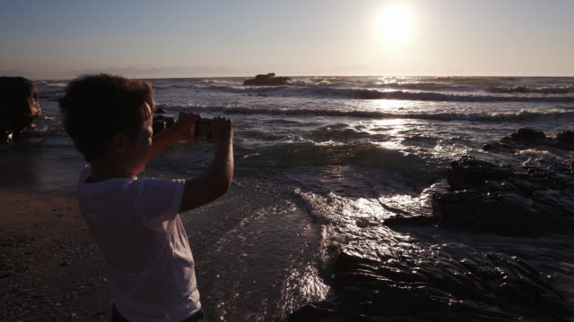 Jóvenes-chico-usando-teléfono-inteligente-para-obtener-una-imagen-en-la-playa-de-Ciudad-del-Cabo,-Sudáfrica