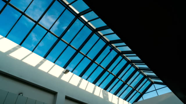 Schwenk-in-der-Glasdecke-des-Einkaufszentrums-auf-einem-Hintergrund-von-Time-Lapse-Licht-der-Sonnenstrahlen-auf-einen-blauen-Himmel