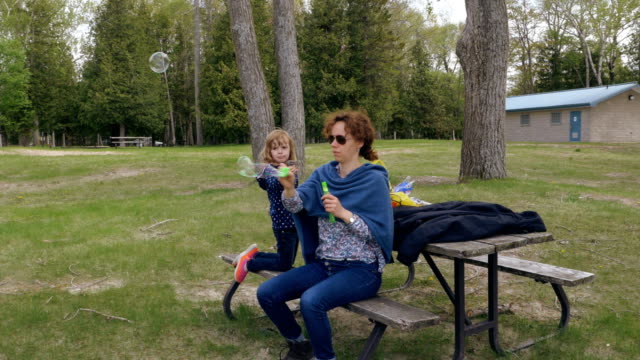 Mutter-und-Tochter-spielen-mit-Seifenblasen-in-einem-Park