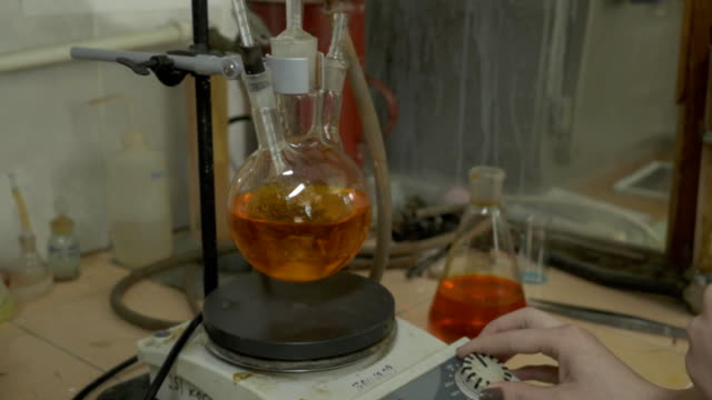 Scientist-mixing-liquids-in-flasks-in-a-research-lab.-Special-equipment-for-mixing-fluids-in-lab.-Intern-mixing-reactants-together-in-the-flask
