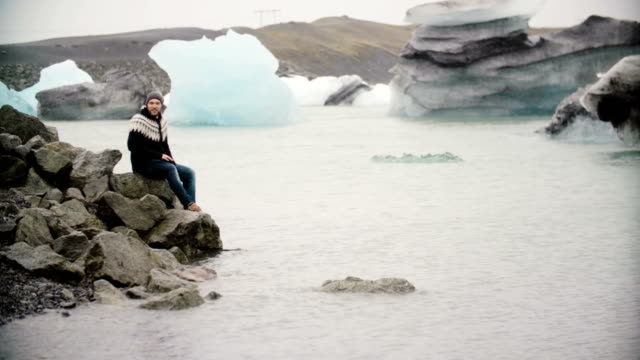 Hübscher-Jüngling-sitzt-auf-dem-Felsen-im-Jokulsalon-Eis-Lagune-in-Island-und-genießen-den-Blick-auf-Gletscher