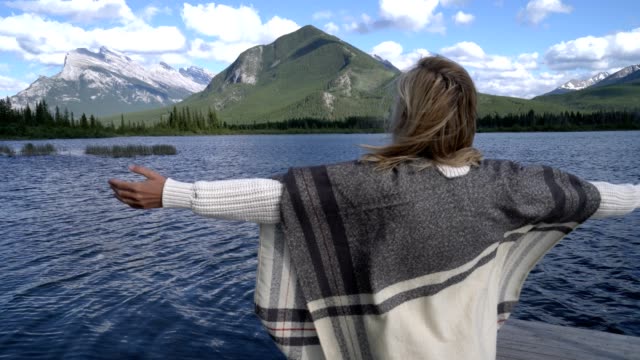 Mujer-joven-de-pie-junto-al-lago-abrazando-la-naturaleza-con-sus-abiertos-brazos