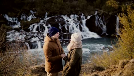 Young-traveling-couple-standing-in-mountains-valley-near-waterfalls-in-Iceland-and-looking-on-each-other,-romantic-date