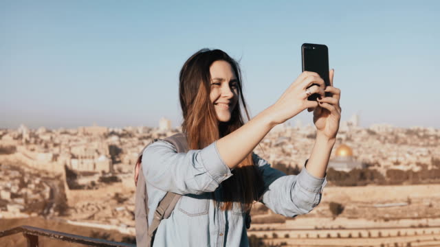 Chica-guapa-toma-selfie-en-el-casco-antiguo-de-Jerusalén.-Linda-chica-local-sonríe-felizes,-toma-fotos.-Panorama-de-Israel-antiguo-4K