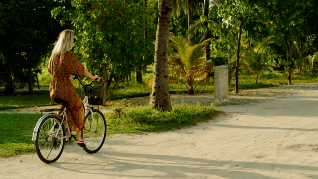 Beautiful-Woman-Wearing-Dress-Rides-Bicycle-on-the-Road-Through-Authentic-Village.-South-Asia-Nature,-Scenic-Forest-Growing-by-the-Road.