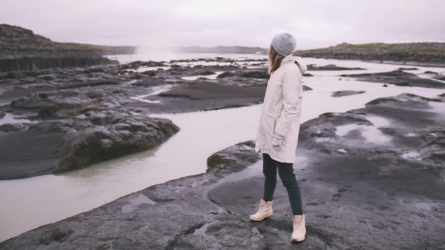 Junge-Frau-in-der-Nähe-von-den-mächtigen-Wasserfall-in-Island