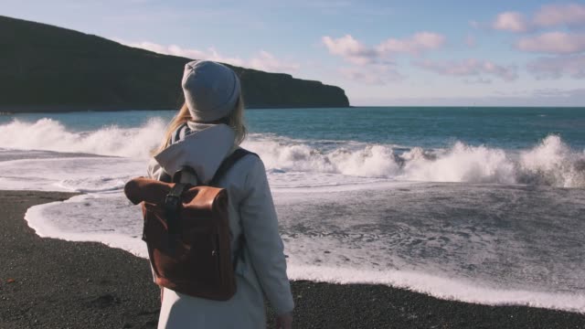 Tourist-woman-with-leather-bagpack-standing-near-the-coastal-landscape-in-Iceland.