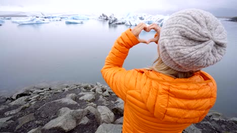 Mujer-joven-haciendo-marco-del-dedo-corazón-forma-en-Laguna-glaciar-en-Islandia