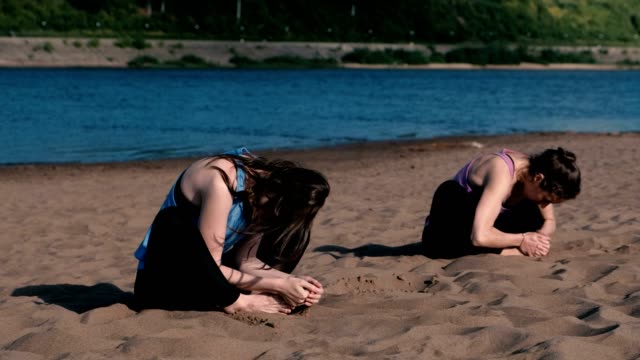 Two-woman-doing-yoga-on-the-beach-by-the-river-in-the-city.-Beautiful-view-in-city.-Individual-training.