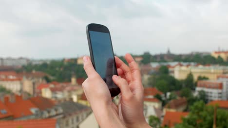 woman-is-looking-on-a-display-of-her-mobile-phone-and-taking-photos-of-top-city-view-in-Prague