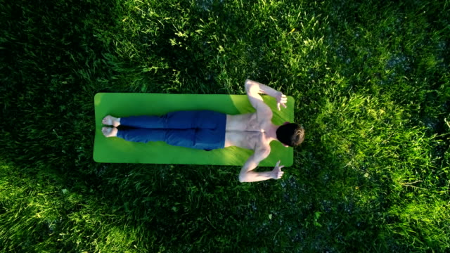 Brünette-Kerl-tut-Yoga-bewegt-sich-auf-dem-grünen-Rasen