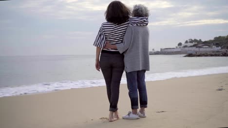 Two-mature-female-tourists-talking-and-hugging-on-seacoast.