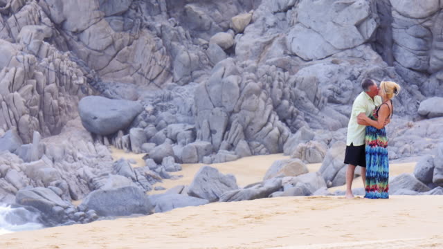 Eine-ältere-paar-küssen-am-Strand-in-vor-großen-Felsen