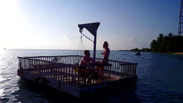 v03828-fliegenden-Drohne-Luftaufnahme-der-Malediven-weißen-Sandstrand-2-Personen-junges-Paar-Mann-Frau-entspannend-auf-sonnigen-tropischen-Inselparadies-mit-Aqua-blau-Himmel-Meer-Wasser-Ozean-4k-schwimmenden-Ponton-Steg-Sonnenbaden-zusammen