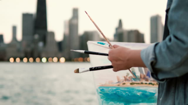 Young-woman-drawing-the-picture-on-the-shore-of-Michigan-lake,-Chicago,-America.-Street-artist-using-brushes-and-paint