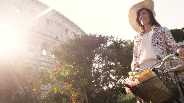 Schöne-junge-Frau-in-die-bunte-Mode-Kleid-allein-zu-Fuß-auf-Hügel-mit-Fahrrad-vor-Colosseum-in-Rom-bei-Sonnenuntergang-mit-Bäumen-attraktives-Mädchen-mit-Strohhut