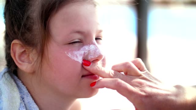 close-up,-the-child,-girls,-severe-sunburn-on-the-face.-Mom-smears-places-of-burns-abundantly-with-a-special-cream.-Mother-applying-sun-protection-cream-to-her-daughter-face