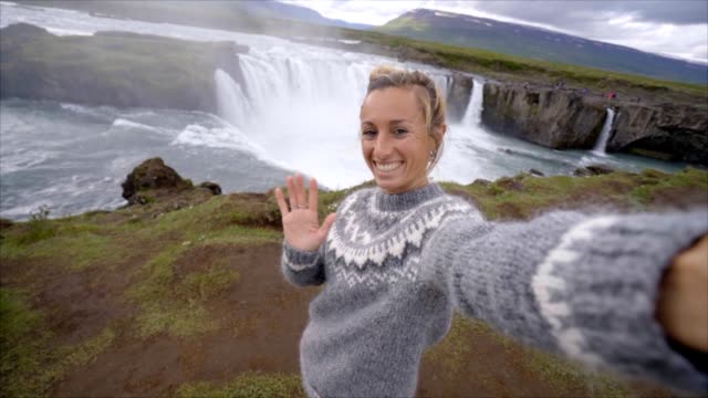 Slow-Motion-junge-Frau-unter-Selfie-Porträt-mit-herrlichen-Wasserfall-in-Island,-Godafoss-fällt.-Die-Leute-reisen-Exploration-Konzept