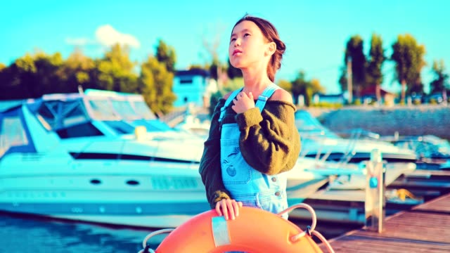 Mädchen-posiert-mit-einem-Rettungsring-am-Kai-von-Booten-und-Yachten
