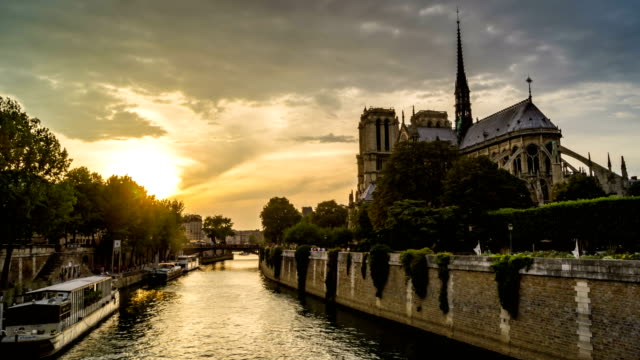 Timelapse-of-Paris-at-sunset,-with-boats-passing-in-front-of-Notre-Dame-de-Paris-cathedral-on-the-Seine-River