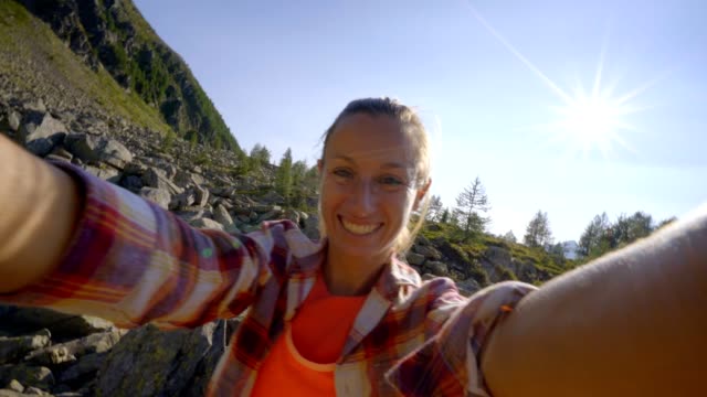 Young-woman-hiking-in-Switzerland-takes-selfie-on-mountain-trail.-Woman-hiker-tasing-selfies-surrounded-by-nature