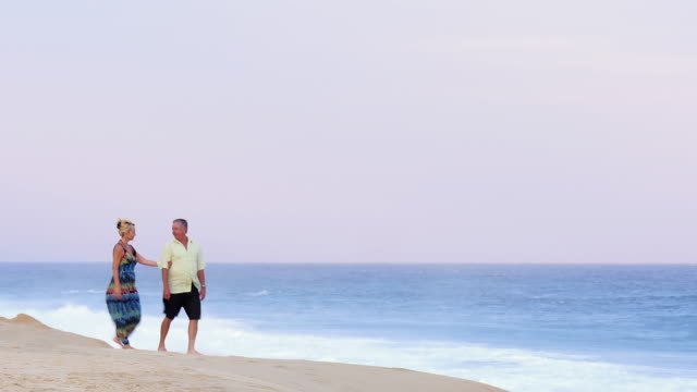An-older-couple-holding-hands-and-walking-down-the-beach-and-embracing