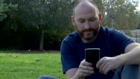 Bearded-man-using-smartphone,-sitting-in-the-park