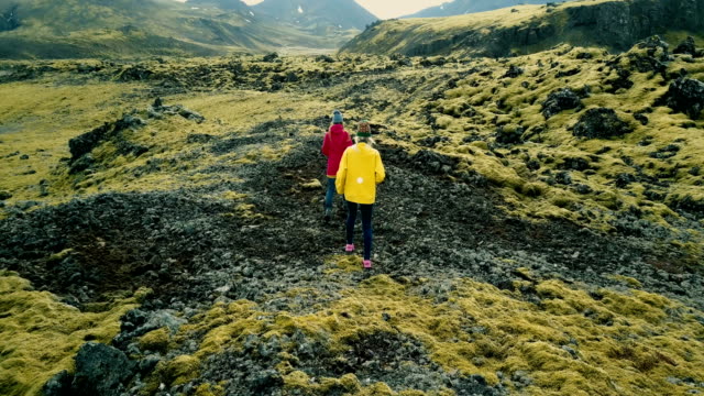 Vista-aérea-de-dos-mujeres-caminando-en-el-campo-de-lava-cubierta-de-musgo-de-Islandia.-Turistas-explorar-el-territorio