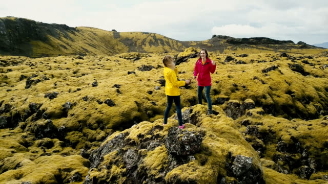 Vista-aérea-de-dos-mujer-de-pie-sobre-la-roca,-caminar-juntos.-Helicóptero-volando-alrededor-de-turista-en-el-campo-de-lava-en-Islandia