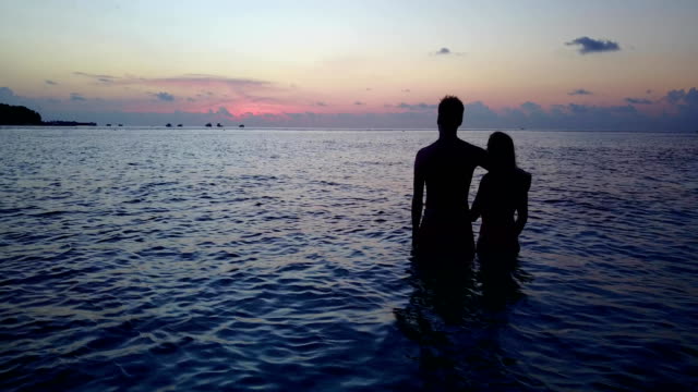 v04175-vuelo-drone-vista-aérea-de-Maldivas-playa-2-personas-pareja-hombre-mujer-amor-romántico-puesta-de-sol-salida-del-sol-en-la-isla-de-paraíso-tropical-soleado-con-cielo-azul-aqua-agua-mar-4k