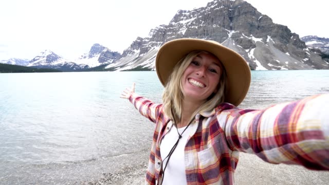 Young-woman-travelling-in-Canada-takes-selfies-by-stunning-mountain-lake-scenery