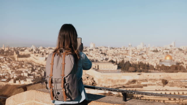 Tourist-girl-takes-photos-of-old-town-Jerusalem.-Girl-with-backpack-walks-to-skydeck-edge.-Capturing-moments.-Israel-4K